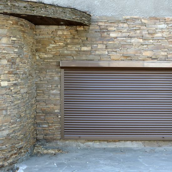 A window with brown metal rolling shutters and wall decoration with artificial stone