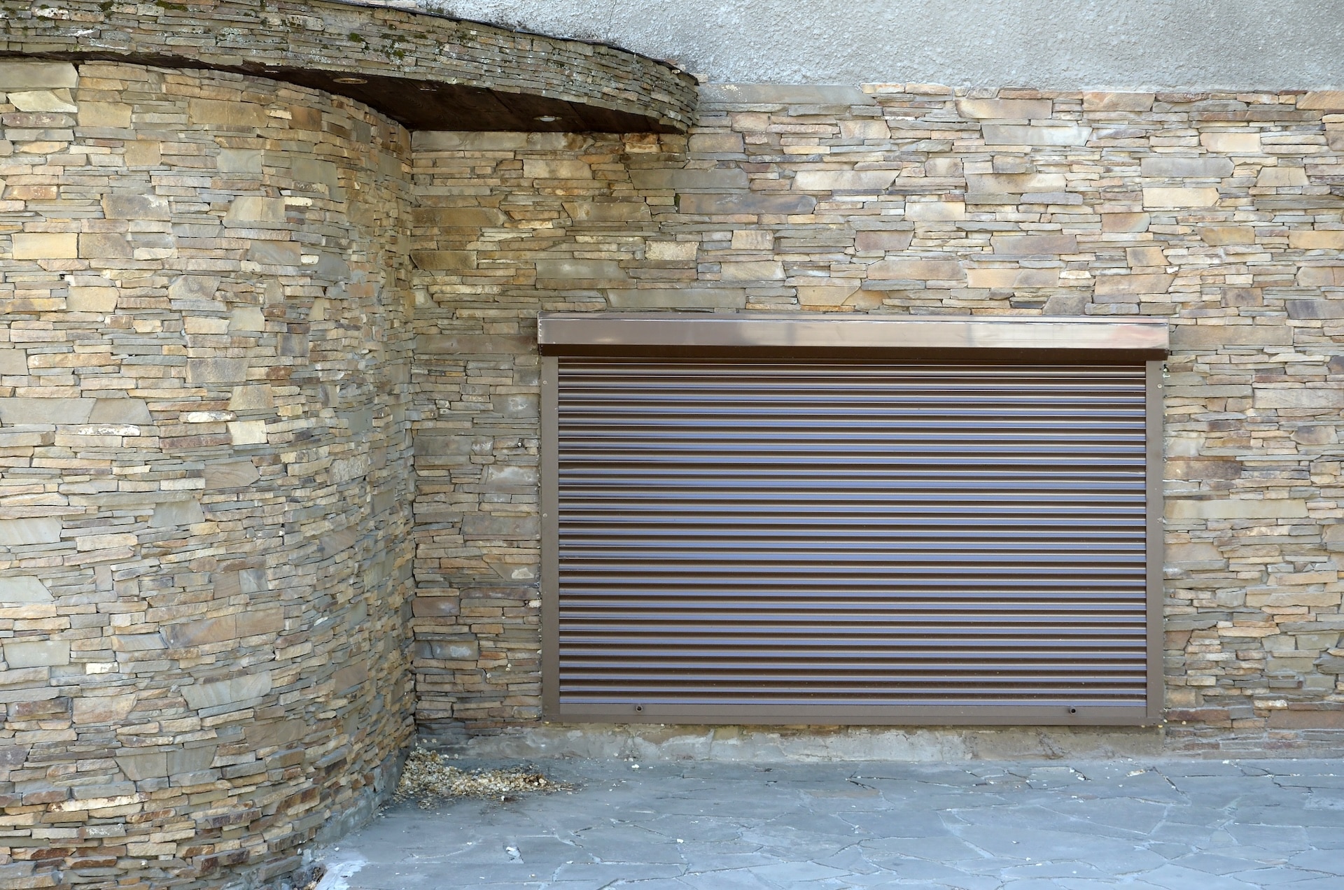 A window with brown metal rolling shutters and wall decoration with artificial stone